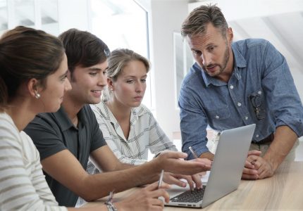 Teacher with group of students working on laptop computer